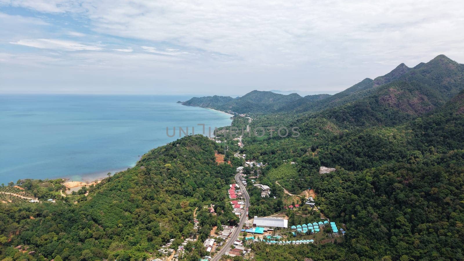 Breathtaking aerial perspective capturing the stunning landscape of tioman island, showcasing lush tropical rainforest, majestic mountains, a winding road, and the picturesque coastline