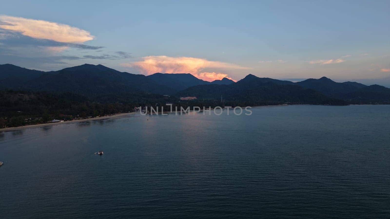 Tranquil coastal scenery featuring calm waters, lush mountains, and a vibrant sunset sky. The peaceful shoreline invites relaxation and contemplation, highlighting nature's beauty