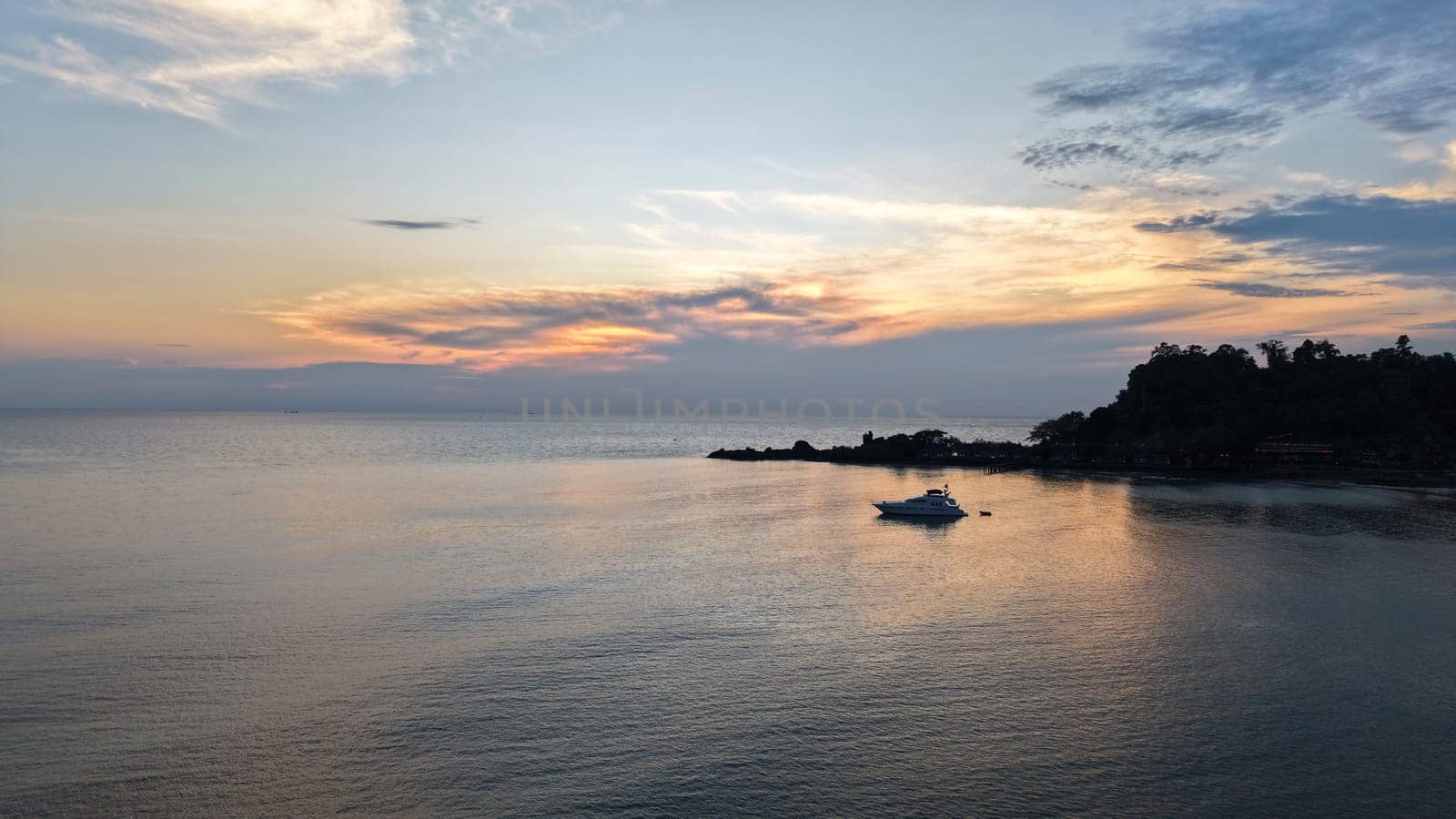 Vibrant sunset colors paint the sky over a tranquil ocean, with a lone yacht anchored near the silhouette of a tropical coastline, creating a serene and picturesque scene