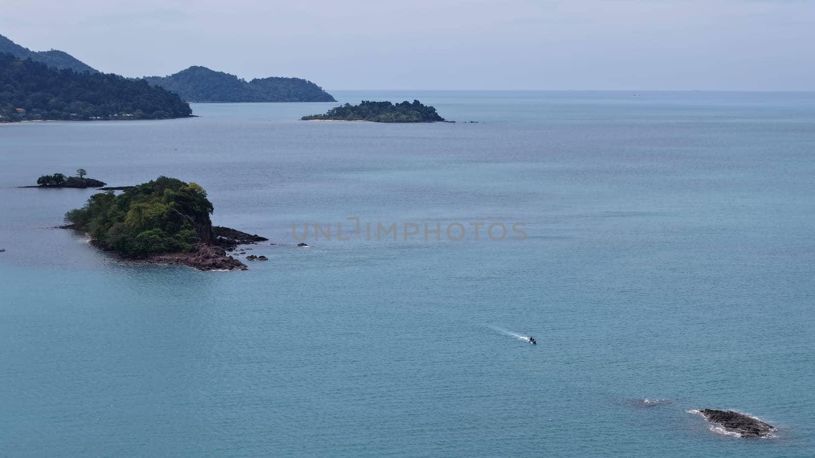 Motorboat is navigating the calm turquoise waters of the sea near tropical islands covered in lush vegetation, creating a serene and idyllic scene