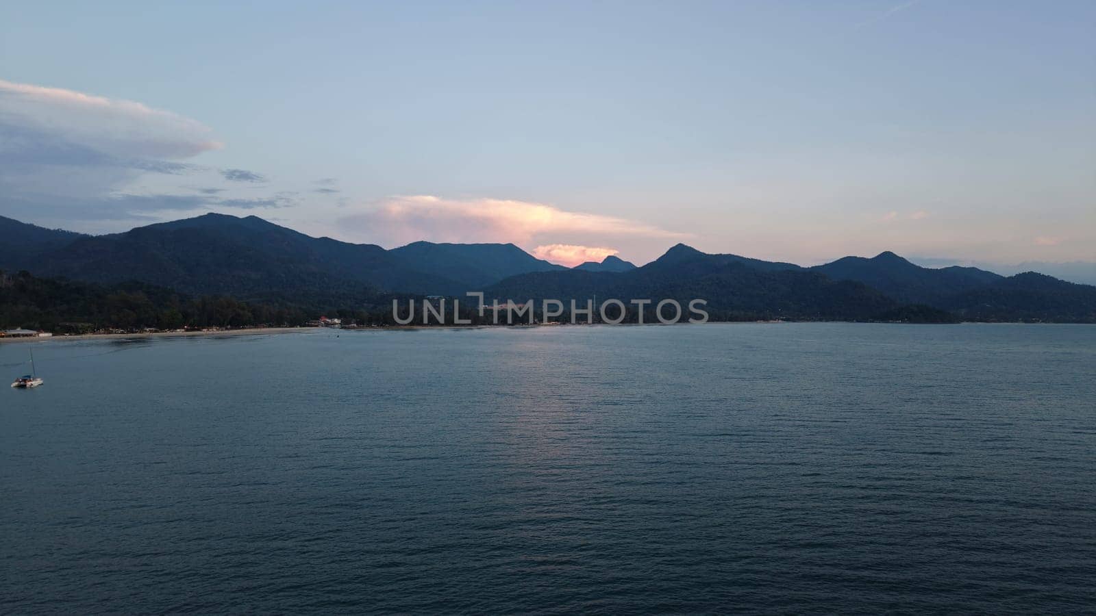 Calm ocean waters reflecting the warm hues of sunset light, framed by majestic mountains and a pristine beach, creating a tranquil and serene atmosphere perfect for relaxation