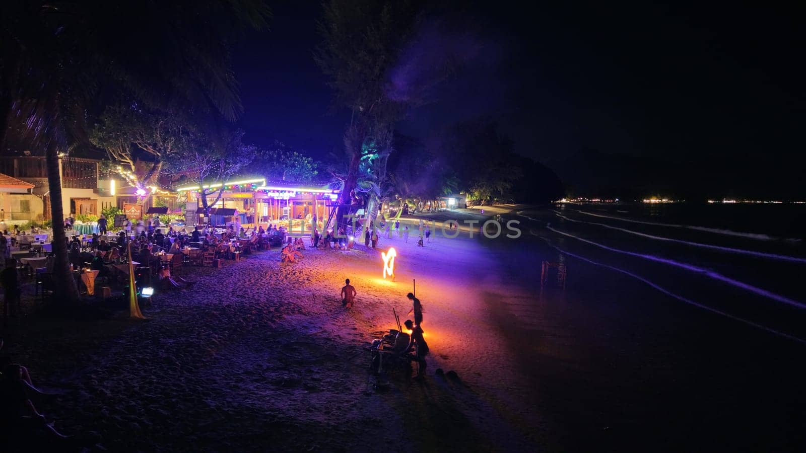 Dining tourists enjoying a mesmerizing fire show at a beach restaurant under the night sky, creating a vibrant and festive atmosphere filled with excitement and tropical charm