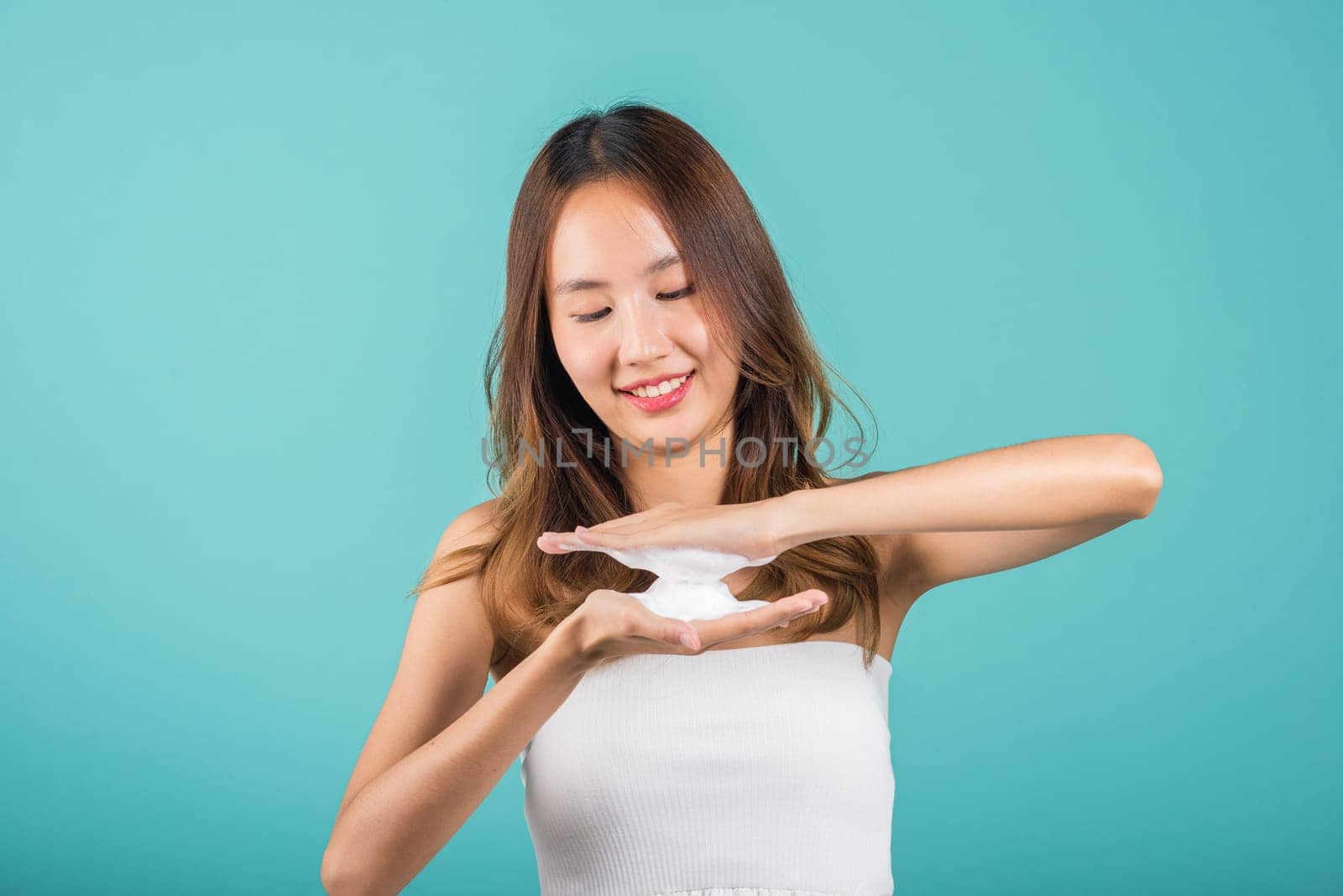 Portrait Asian young woman hands are adorned with white foam mousse studio shot isolated on blue background, beautiful female holds a cleansing foam near her face, Cosmetics beauty skincare
