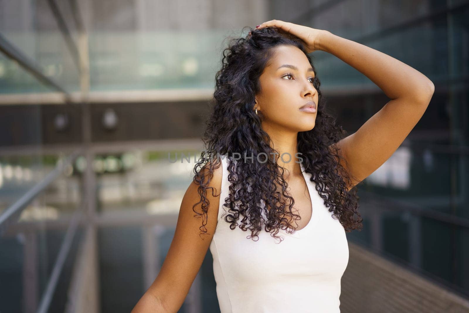 A young woman with beautiful curly hair poses gracefully against stunning architecture, showcasing her poise and confidence in a captivating scene that holds the viewers attention