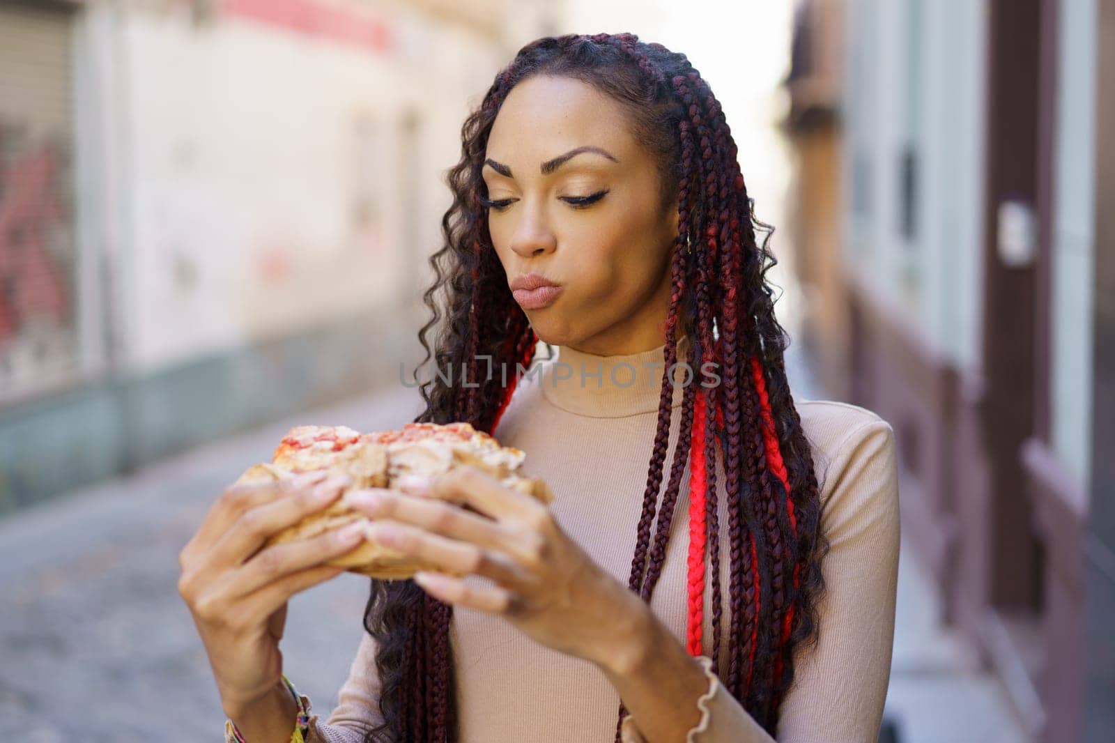 A woman is taking her time savoring a delicious slice of pizza while sitting on a bench in a vibrant, colorful street, perfectly showcasing the essence of urban life and the joy of food enjoyment