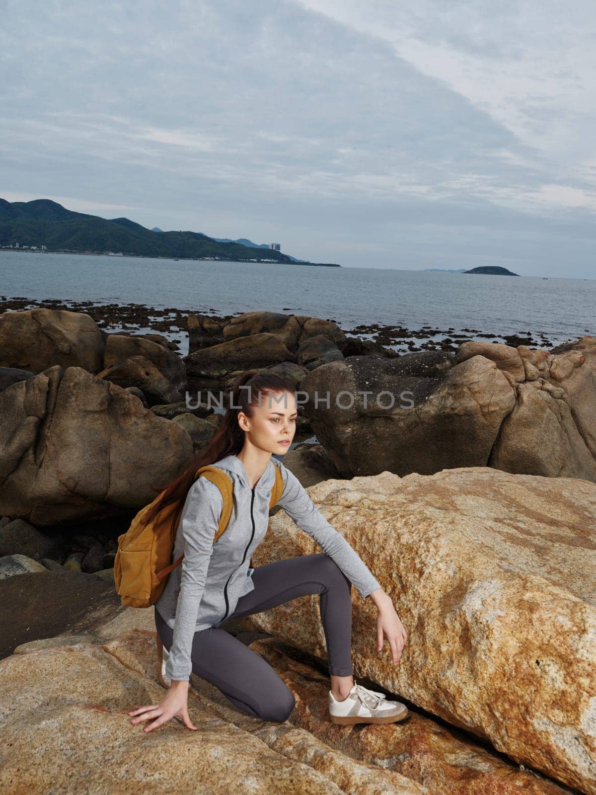 A young woman in activewear squats on a rocky beach, embodying determination and a love for nature Capturing the essence of adventure and healthy living, this image is perfect for fitness, wellness, and lifestyle themes