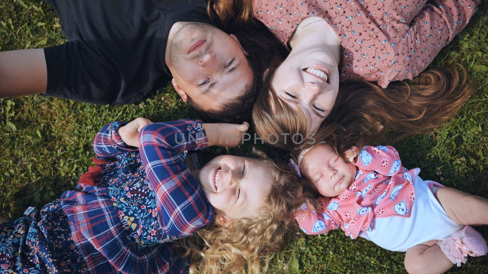Cheerful family members forming circular huddle on verdant lawn, sharing warm embraces and bright smiles during outdoor bonding moment