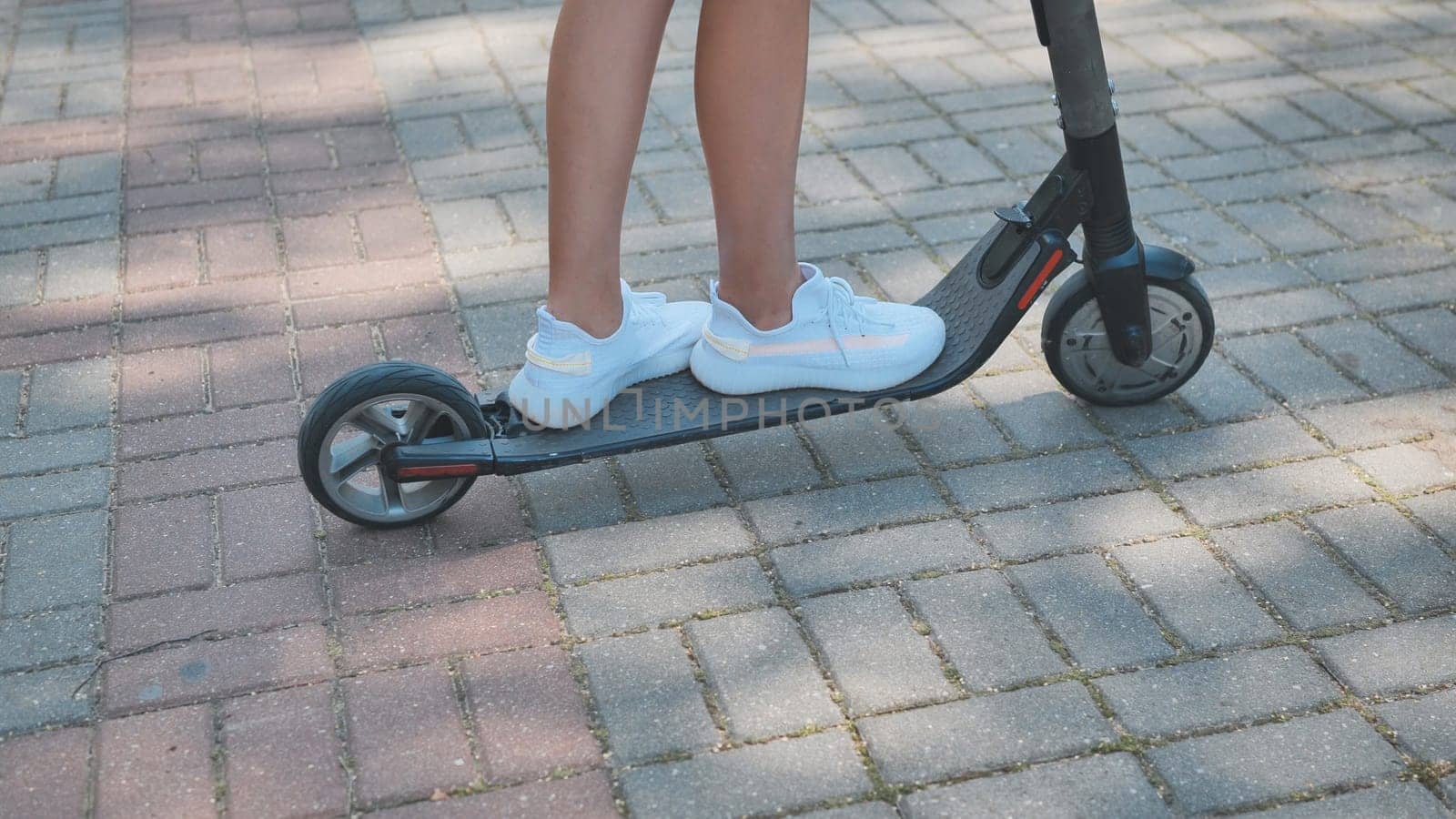 Close up of legs and feet of teen girl riding electric scooter in park during summer, enjoying sustainable transportation