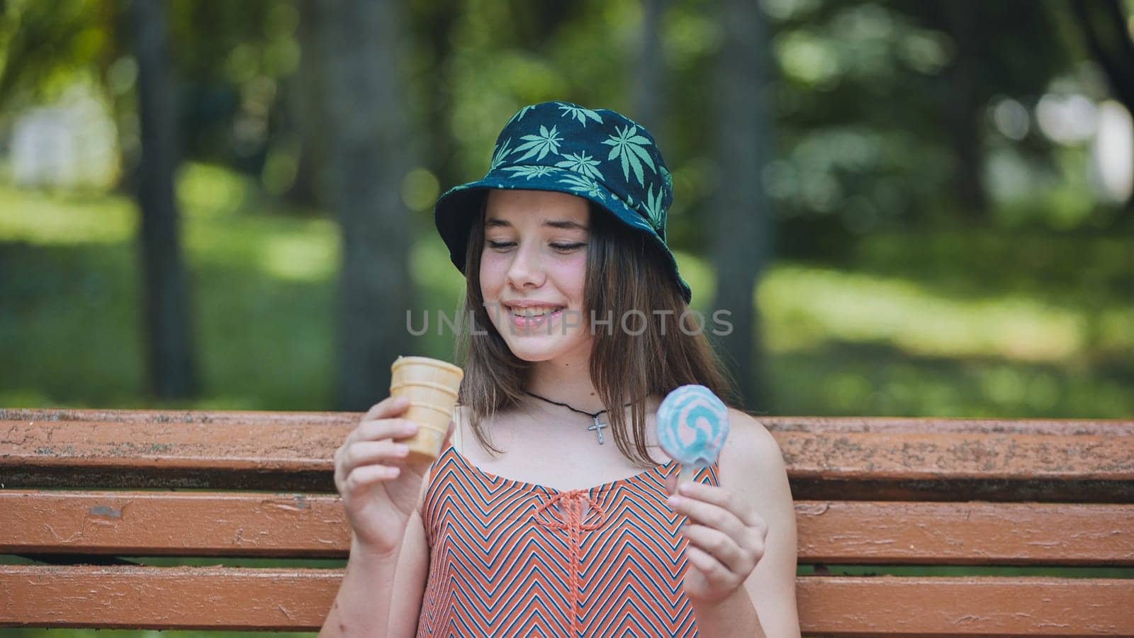 Teenage girl relaxing on park bench, savoring colorful ice cream and lollipop during sunny afternoon