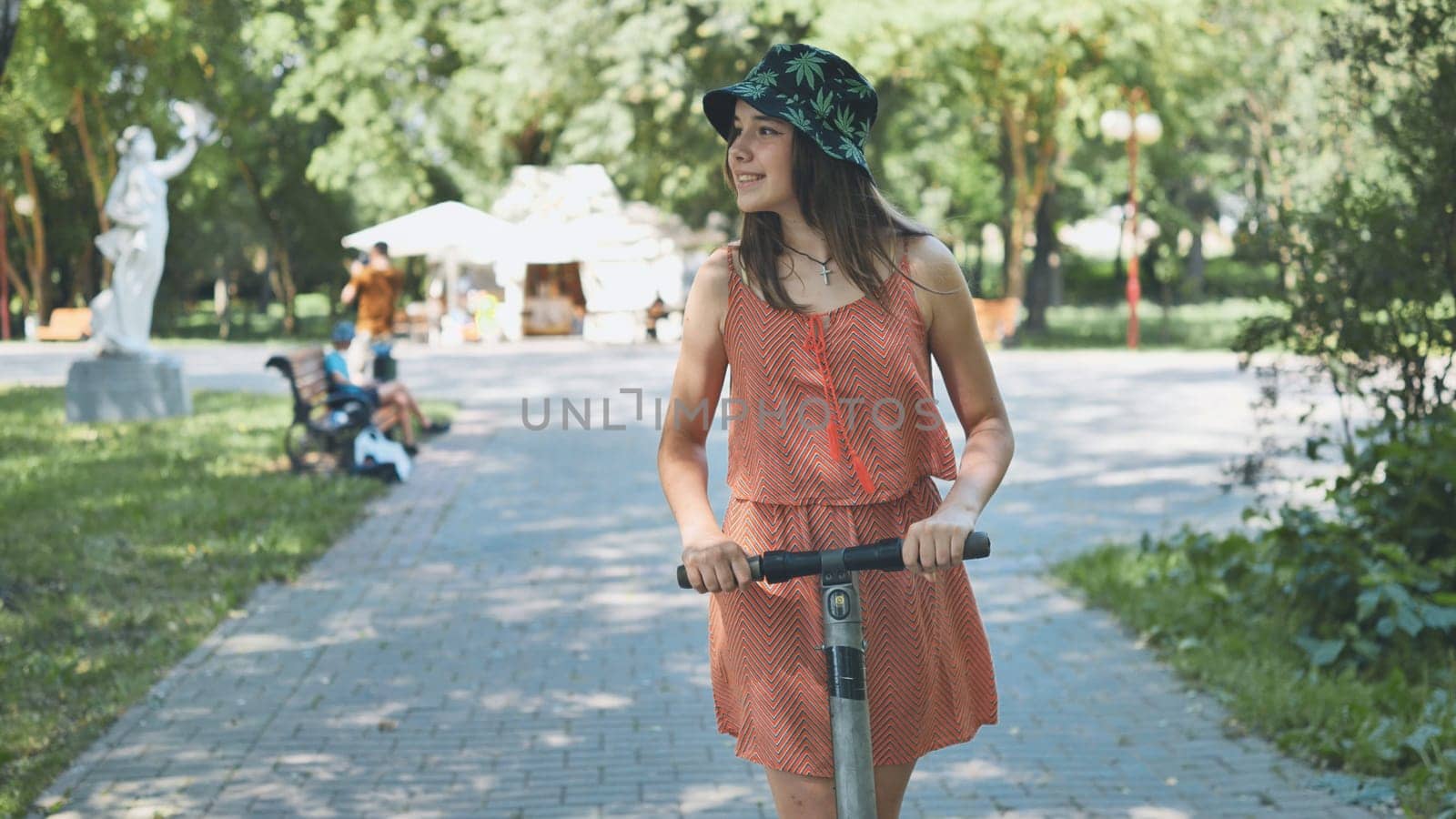 Woman riding electric scooter through sunny park, experiencing eco friendly urban mobility with carefree attitude