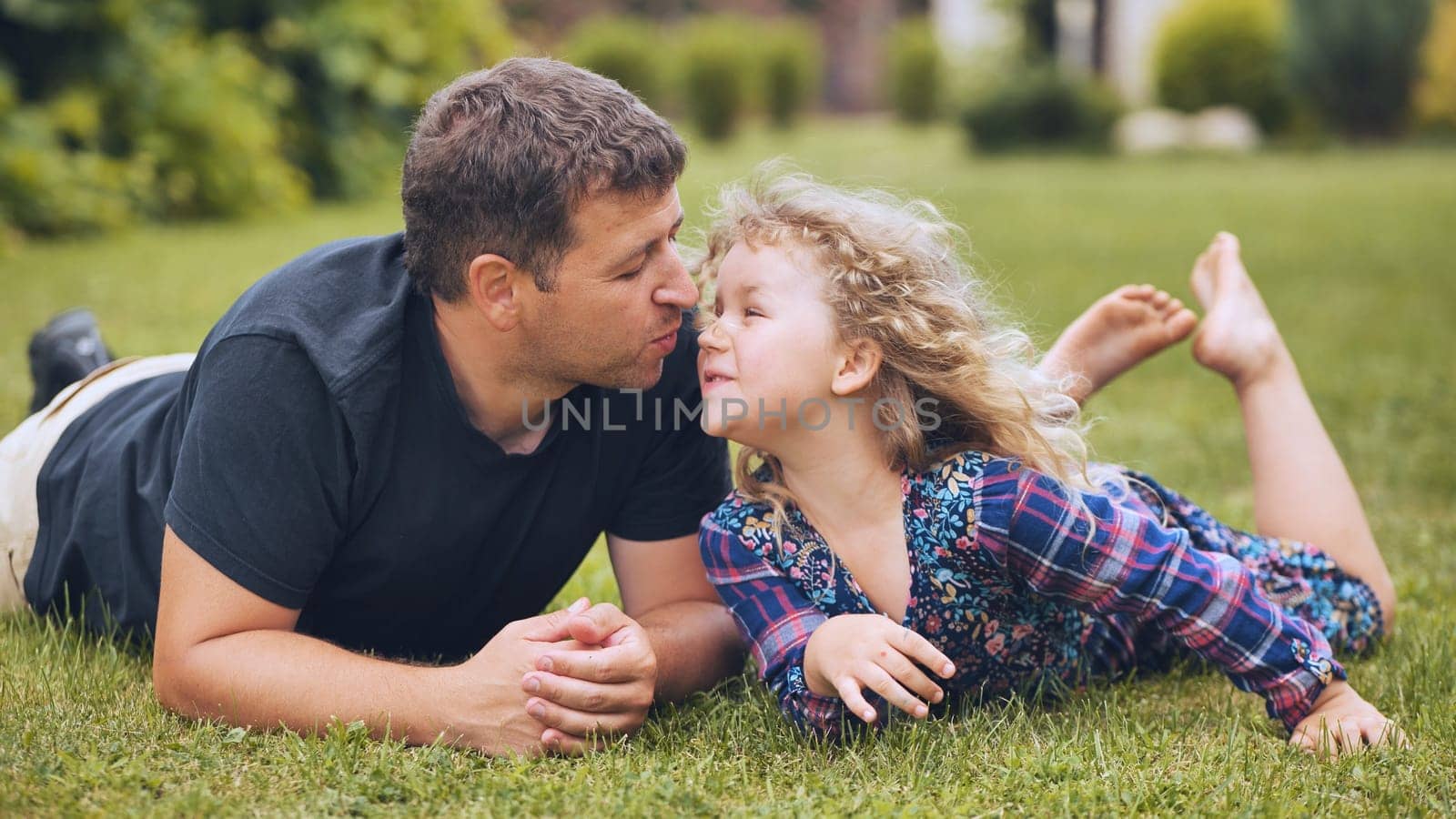 Family bonding moment, father and daughter lying on lush grass, sharing gentle affection and warmth during peaceful outdoor connection