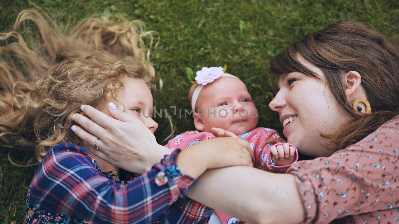 Mother and daughters lying on the grass, enjoying a joyful family day filled with love, laughter, and tender moments in nature