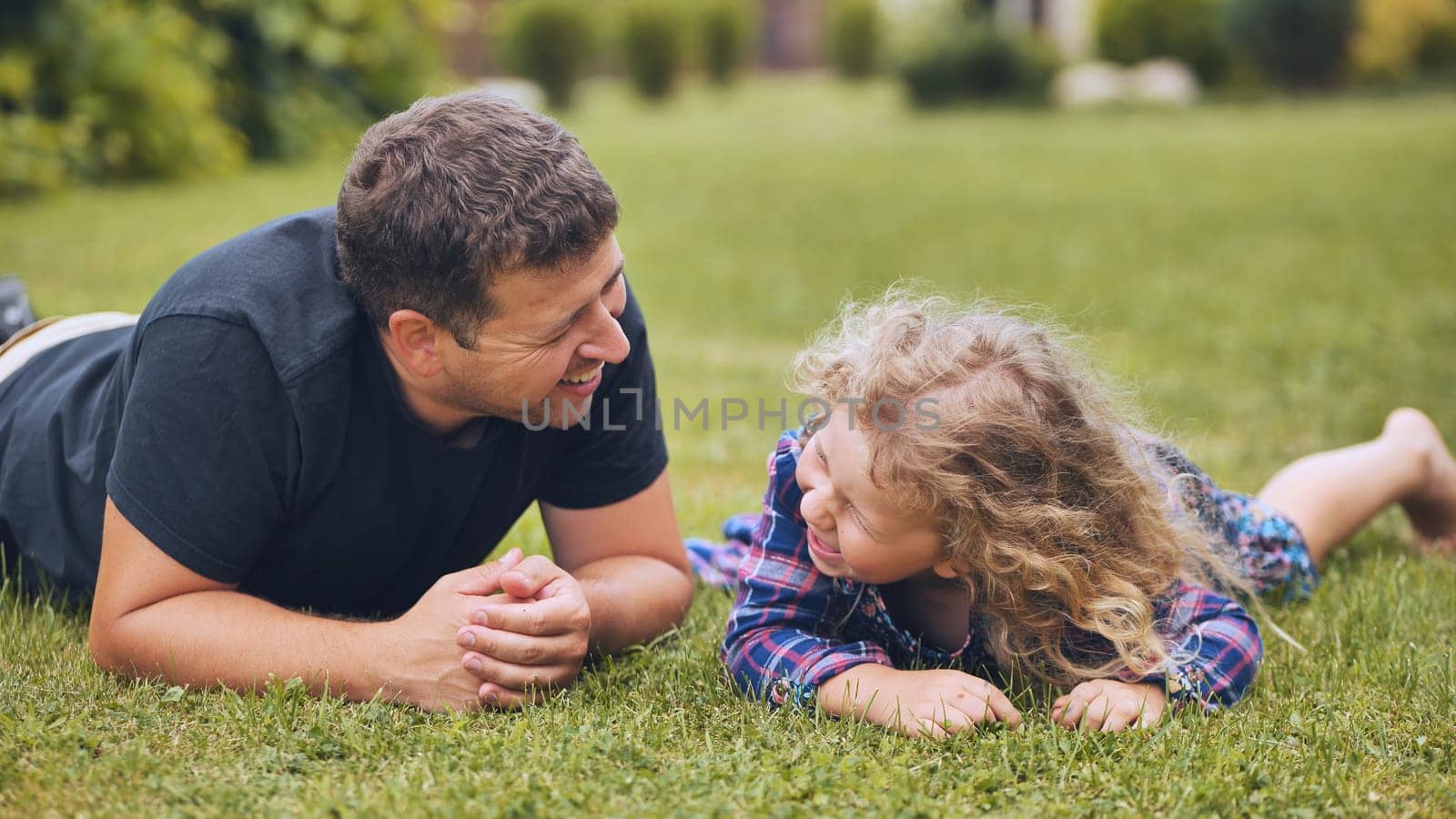 Father and daughter enjoying a playful moment together, lying on the grass and sharing laughter on a sunny day
