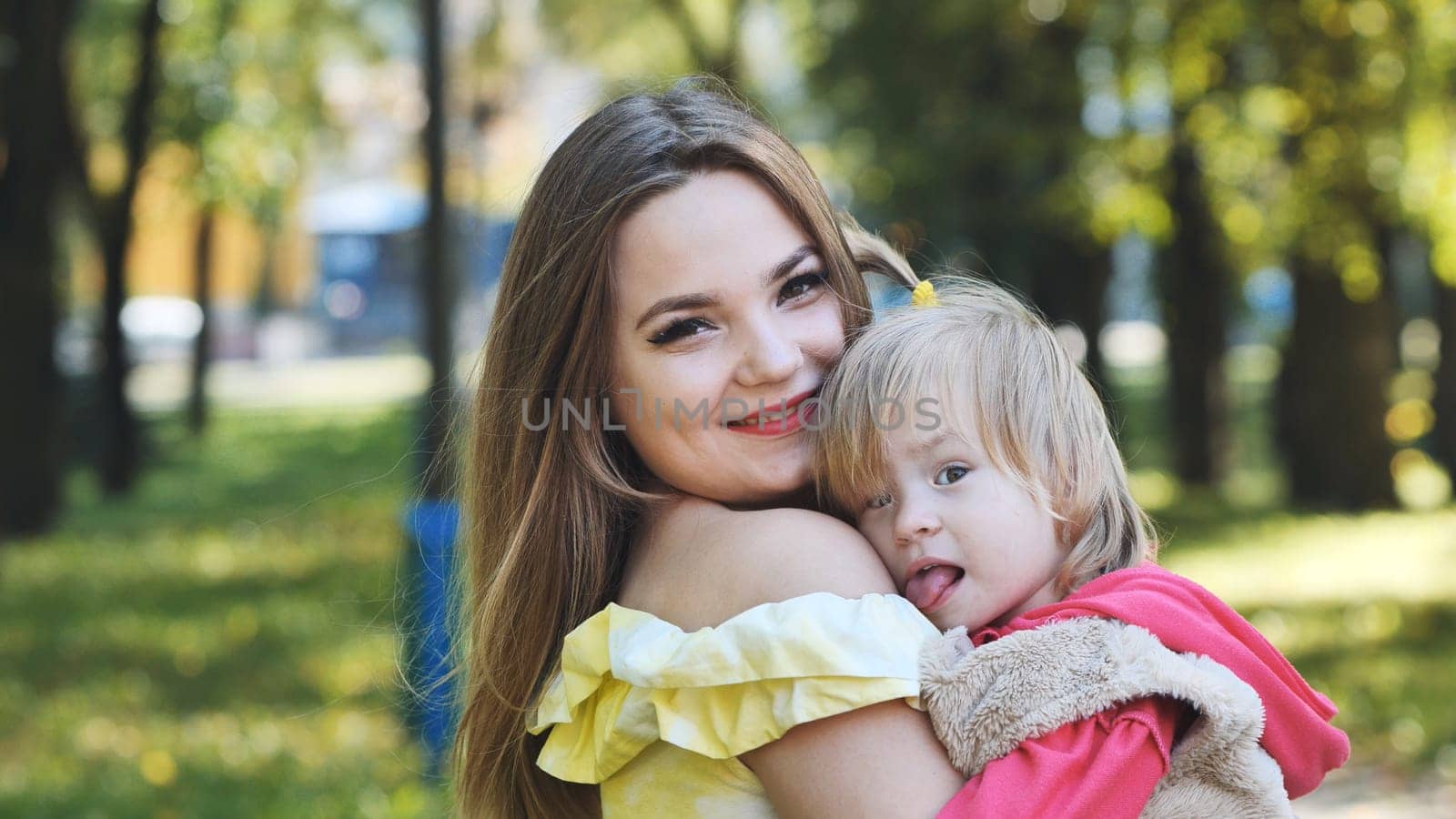 Happy mother holding her daughter in a park, sharing joyful moments and embracing the warmth of a sunny autumn day together
