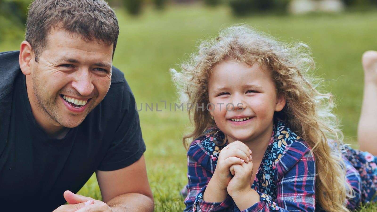 Father and daughter relaxing on grassy lawn, sharing joyful moment, laughing together under bright sunlight during outdoor family time