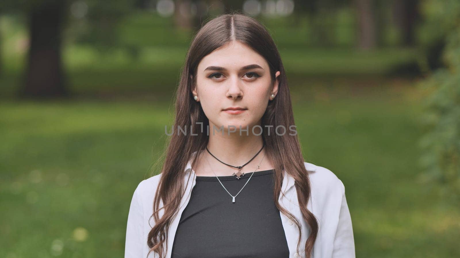 Portrait of a beautiful young georgian woman posing gracefully in a vibrant green park, surrounded by serene nature and blooming trees