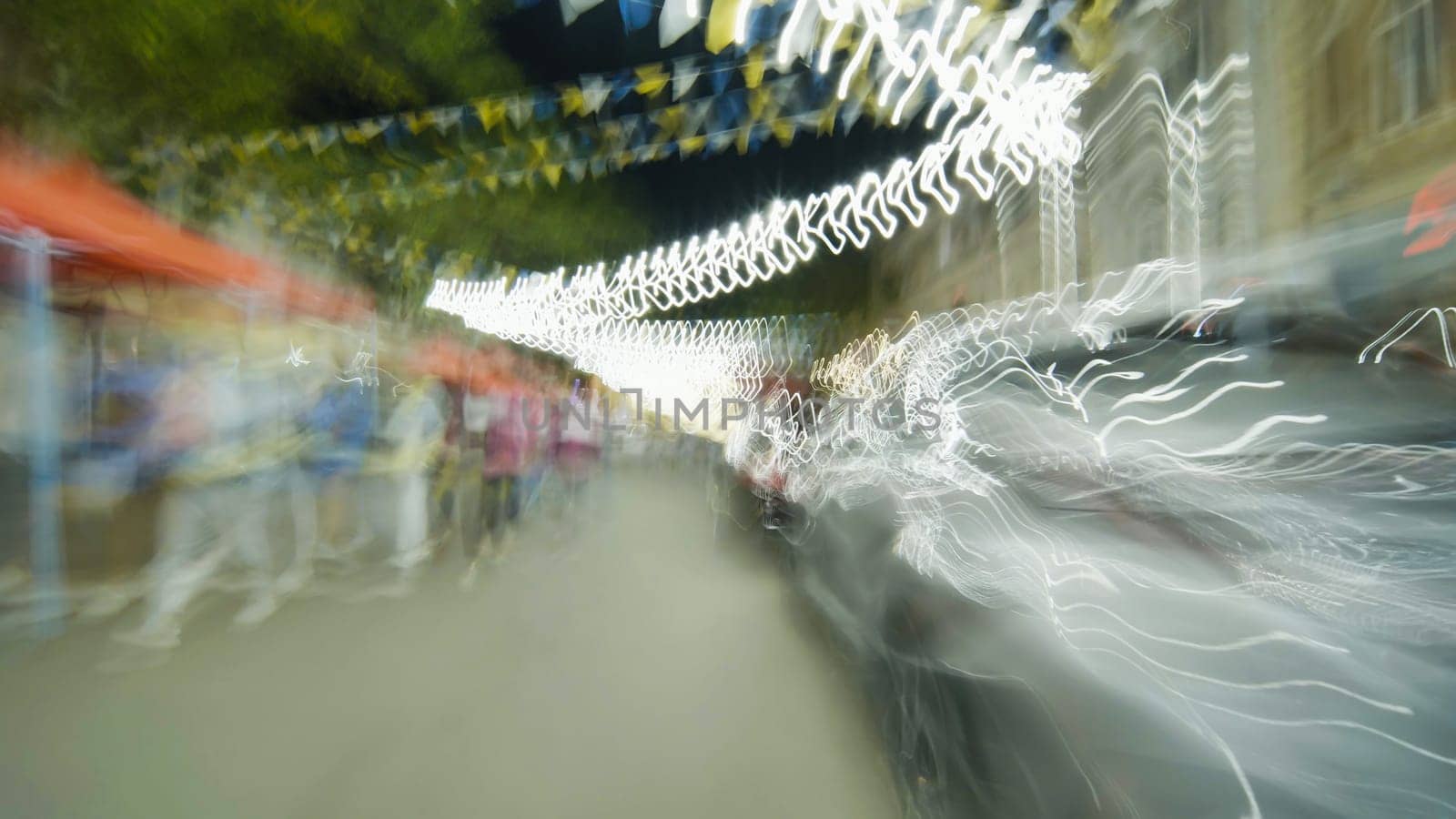 Light trails created by moving cars illuminating a night market with festive flags overhead