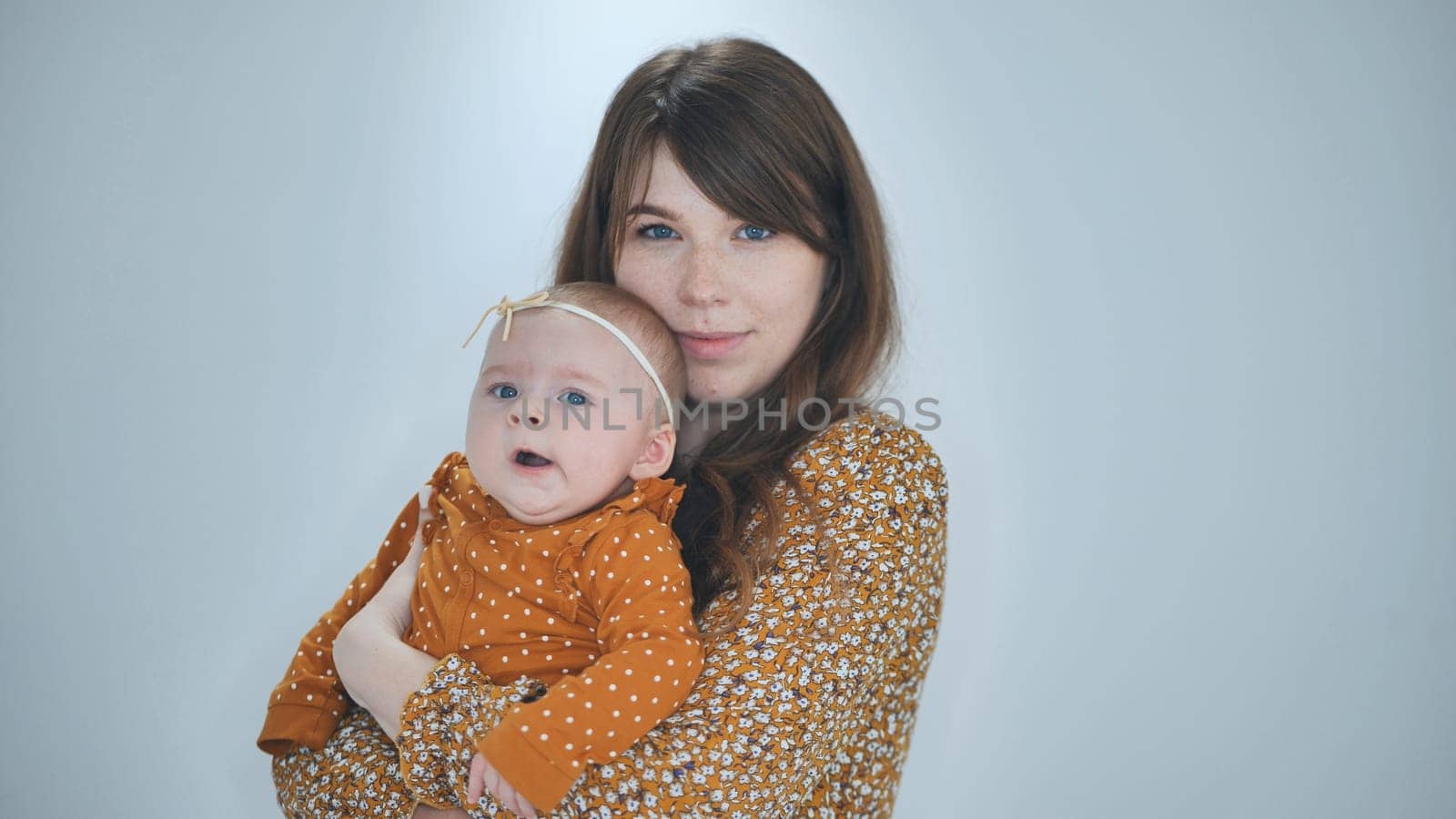 Studio portrait of a mother holding her baby girl, both wearing matching orange outfits, conveying a sense of love and connection