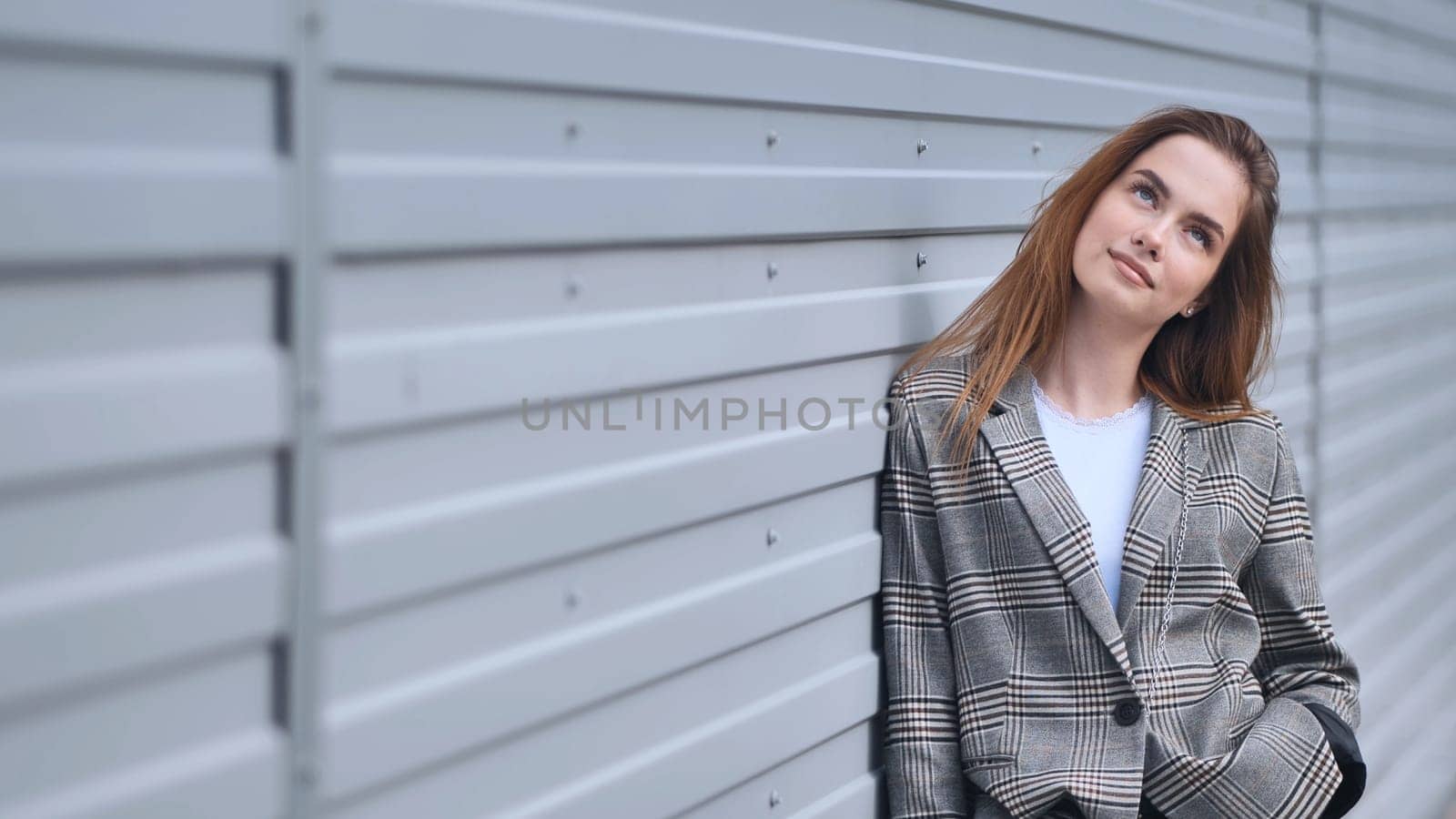 Professional female executive wearing plaid blazer, gazing upward, reflecting near sleek metallic surface with contemplative expression