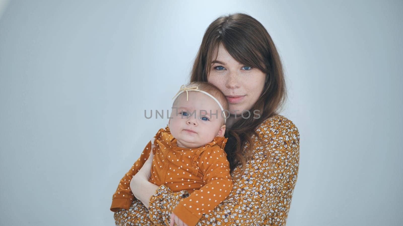 Studio portrait of a loving mother holding her baby daughter, both wearing matching patterned clothes in shades of orange
