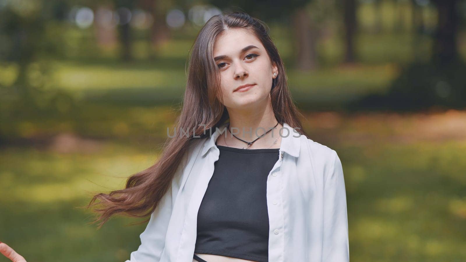 Portrait of a young georgian woman posing in a green park, wearing a white shirt and black top