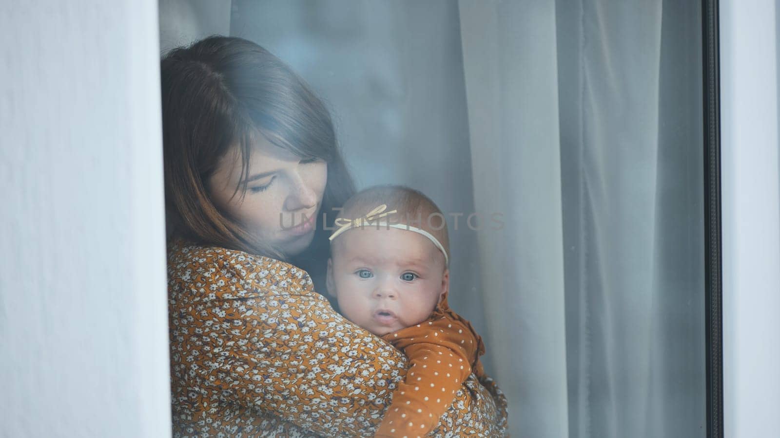 Loving mother embracing newborn daughter near sunlit window, sharing intimate bonding moment of tenderness and maternal warmth