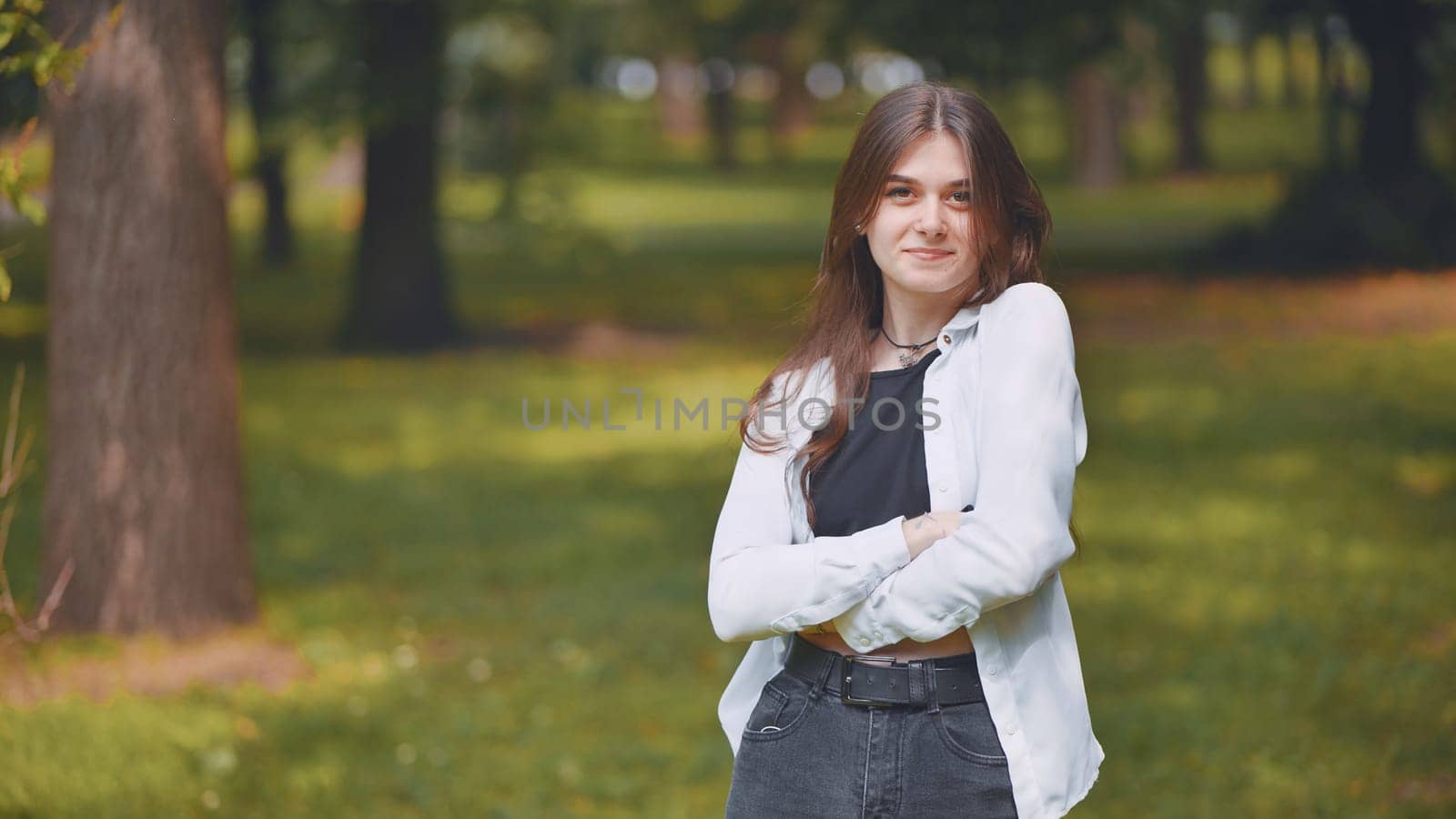 Portrait of a young georgian woman standing with crossed arms in a lush green city park, enjoying the tranquility of nature