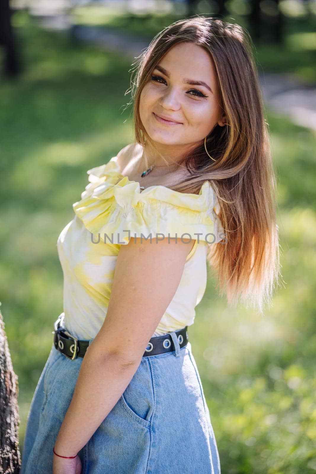 Portrait of a smiling teenage girl posing in a park, wearing a yellow top and a denim skirt