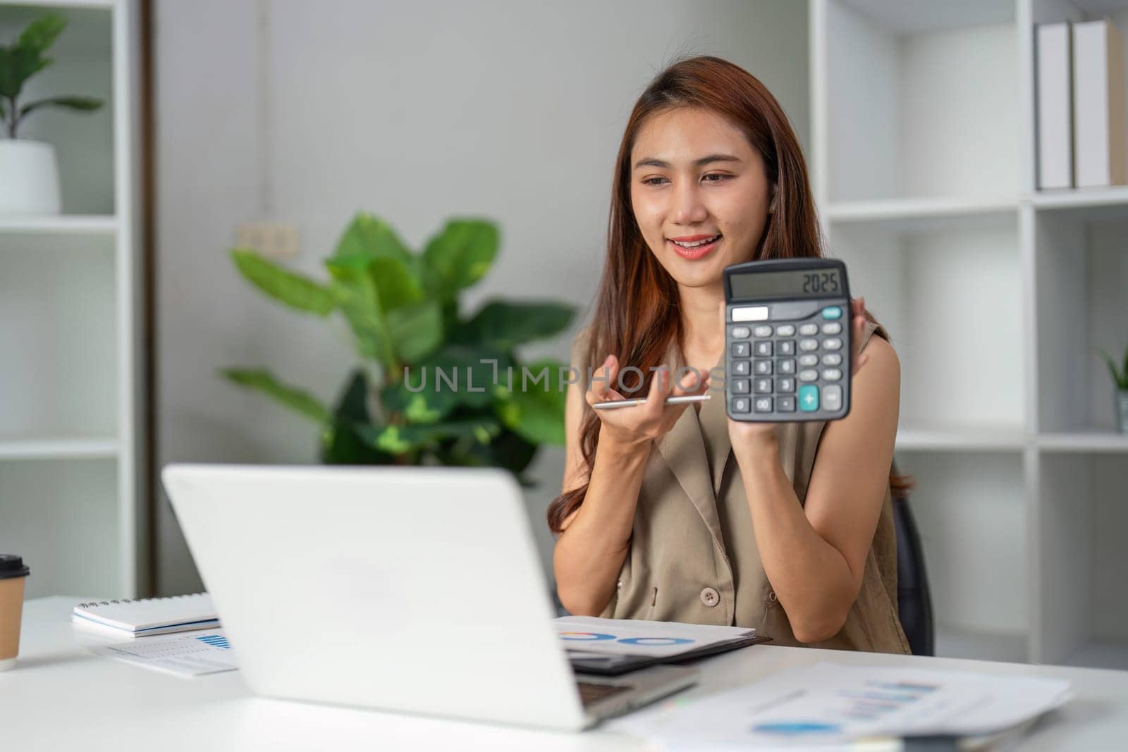 Displaying her calculator, a woman discusses financial data during a virtual work meeting, demonstrating her analytical proficiency.