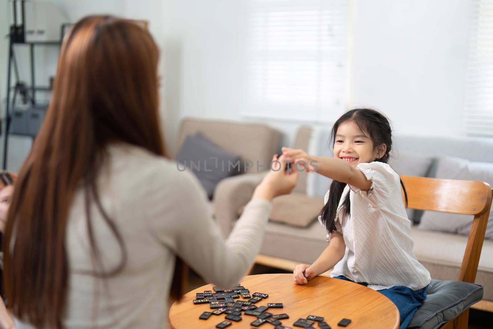 The young girl examines the game pieces carefully, demonstrating focus and the joy of learning through play with her supportive mother.