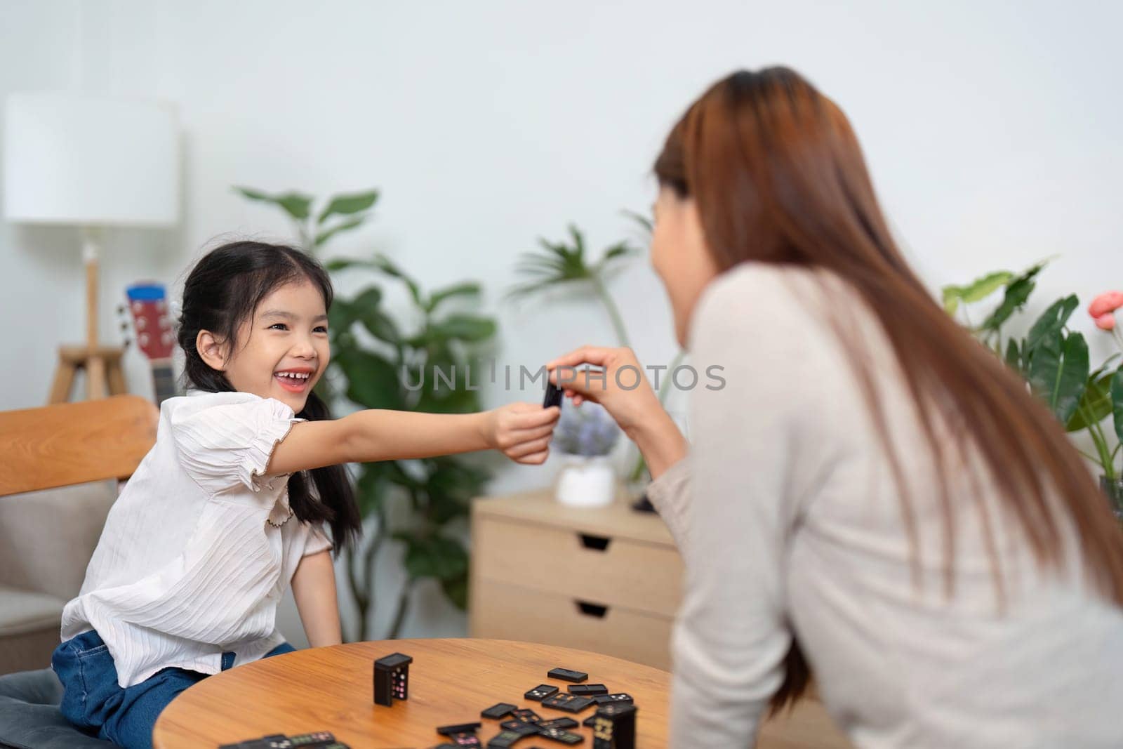 A mother and her daughter enjoy quality time together, engaging in a board game. The girl gleefully hands over a game piece, highlighting their playful interaction and bonding.