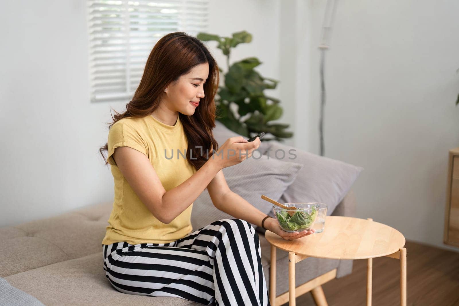 A young woman enjoys a fresh salad while talking on the phone, reflecting a modern lifestyle that prioritizes health and connection.