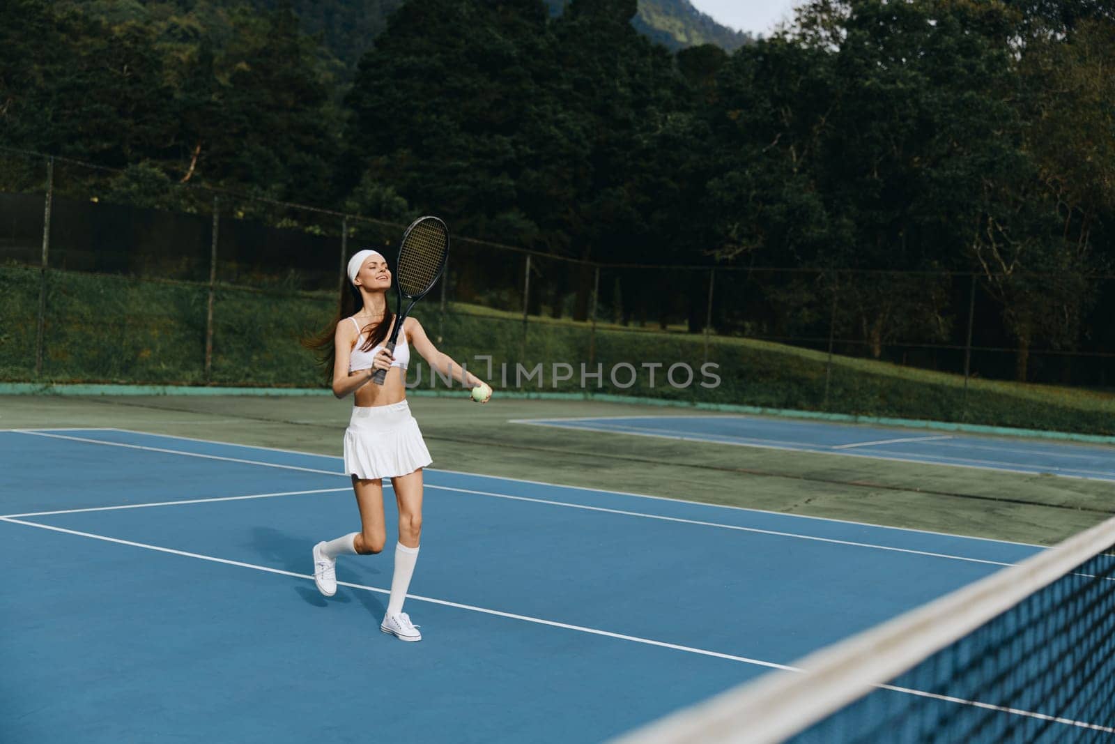 Joyful female tennis player dressed in white sports attire, playing on a bright blue court, showcasing athleticism and the happiness of outdoor sports in a vibrant natural setting