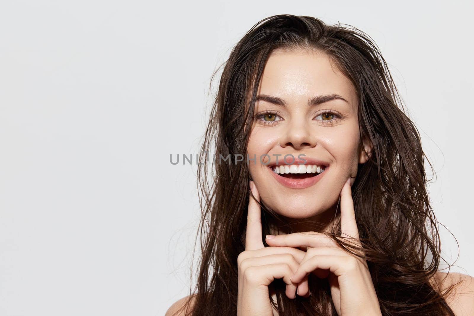 A cheerful young woman with wet, long hair smiles brightly, showcasing her natural beauty and confidence The subtle light background enhances her joyful expression, perfect for wellness themes