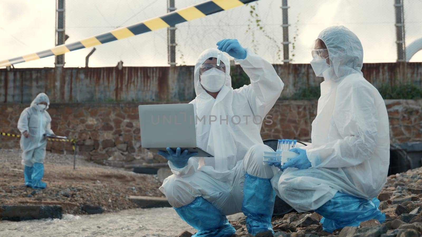 Ecologist sampling water from the river with test tube and save data to laptop computer, Biologist in a protective suit and mask collects sample of waste water from industrial, problem environment