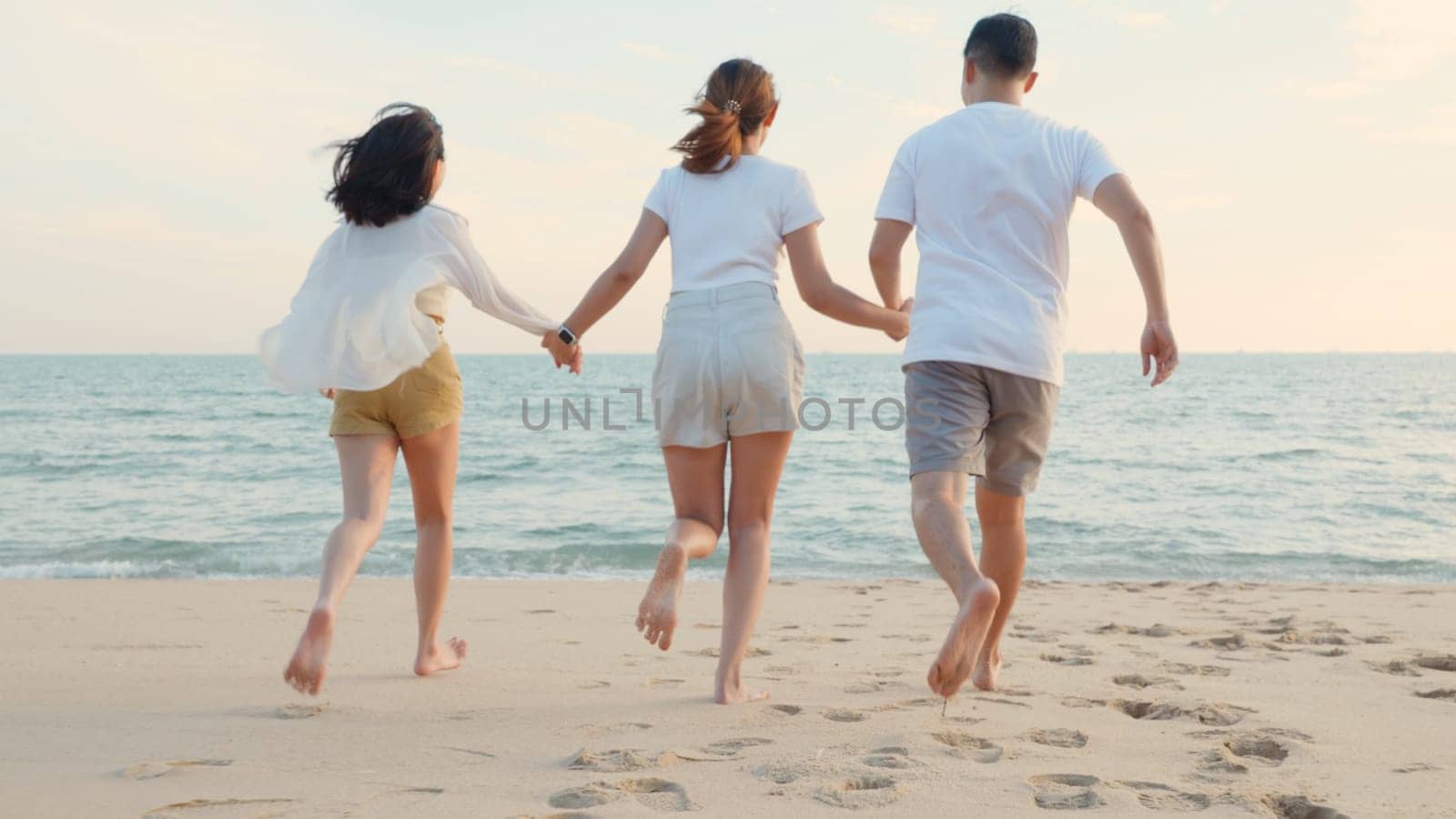 Happy friends holding hands running enjoy life funny and freedom on sand at beach together to sea in holiday vacation time at sunset, Young Asian group woman and man in summer travel, people lifestyle