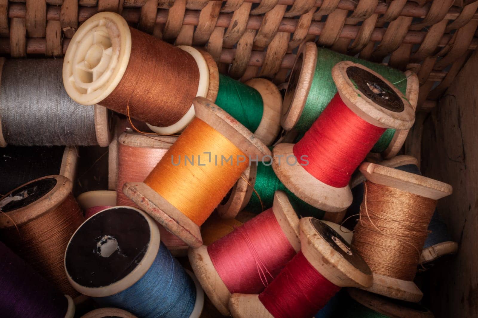 Collection of multicolored thread spools with a vintage look, stored in a rustic basket. Perfect for themes related to sewing, crafting, handmade products, textile work, and traditional artisan techniques.