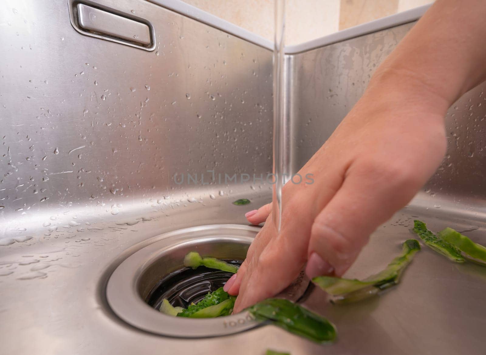 Woman using a garbage disposal to get rid of cucumber peels in a modern sink.