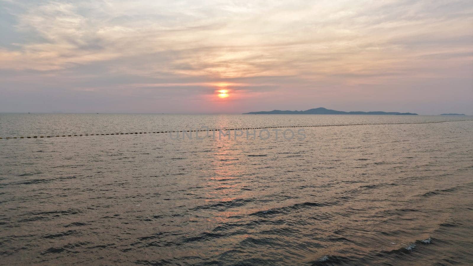 Golden hues of sunset paint the sky over a tranquil ocean, its surface reflecting the light as distant islands silhouette against the horizon, creating a serene and picturesque seascape