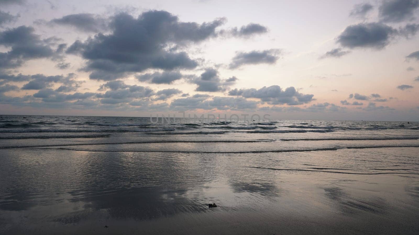 Soft waves gently roll onto the sandy shore as the sun dips below the horizon, painting the sky with vibrant hues of orange and pink during a serene sunset at the beach