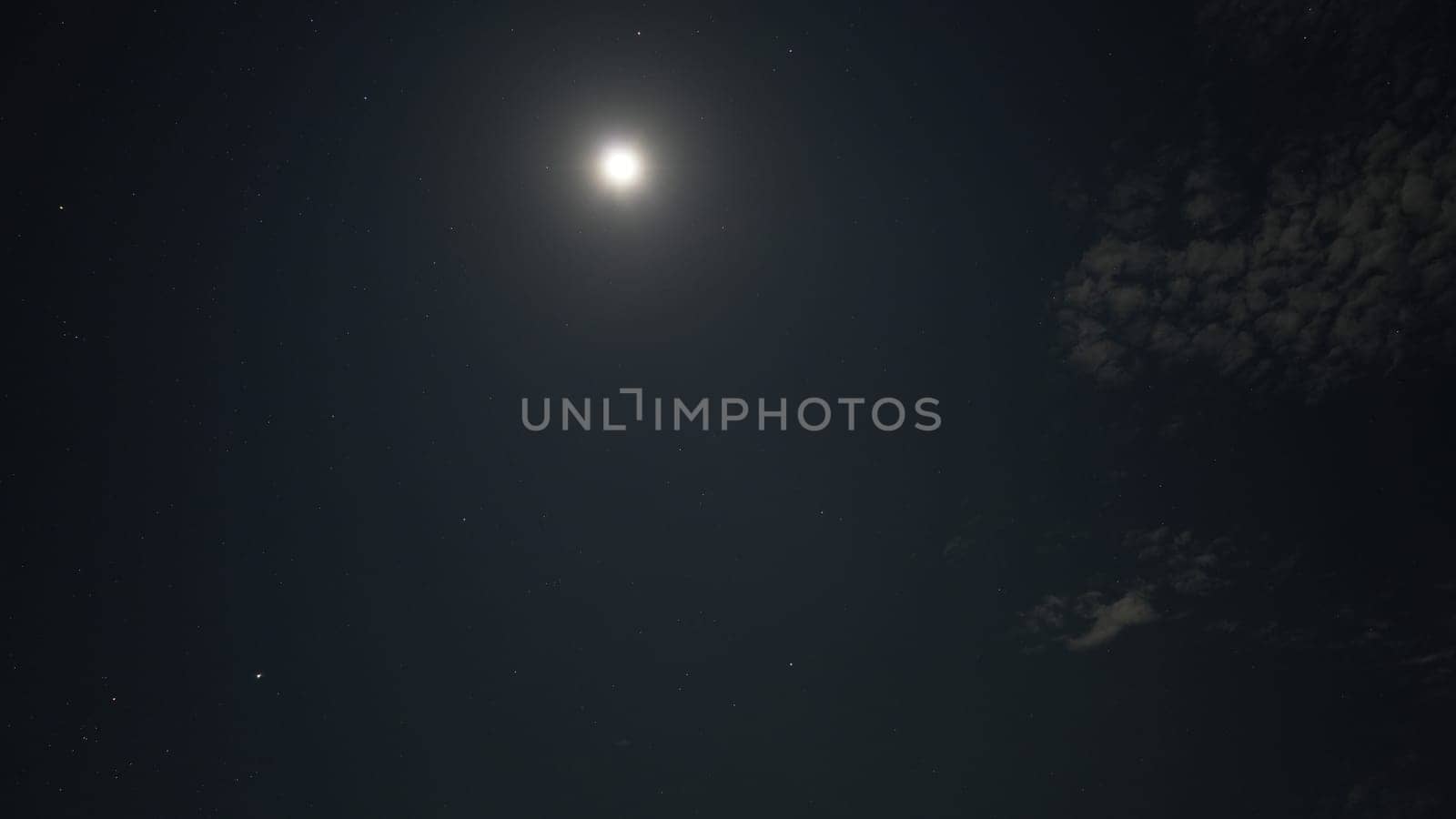 Moon shining brightly in a dark night sky, surrounded by twinkling stars and wispy clouds, creating a tranquil and serene atmosphere of celestial beauty and calmness