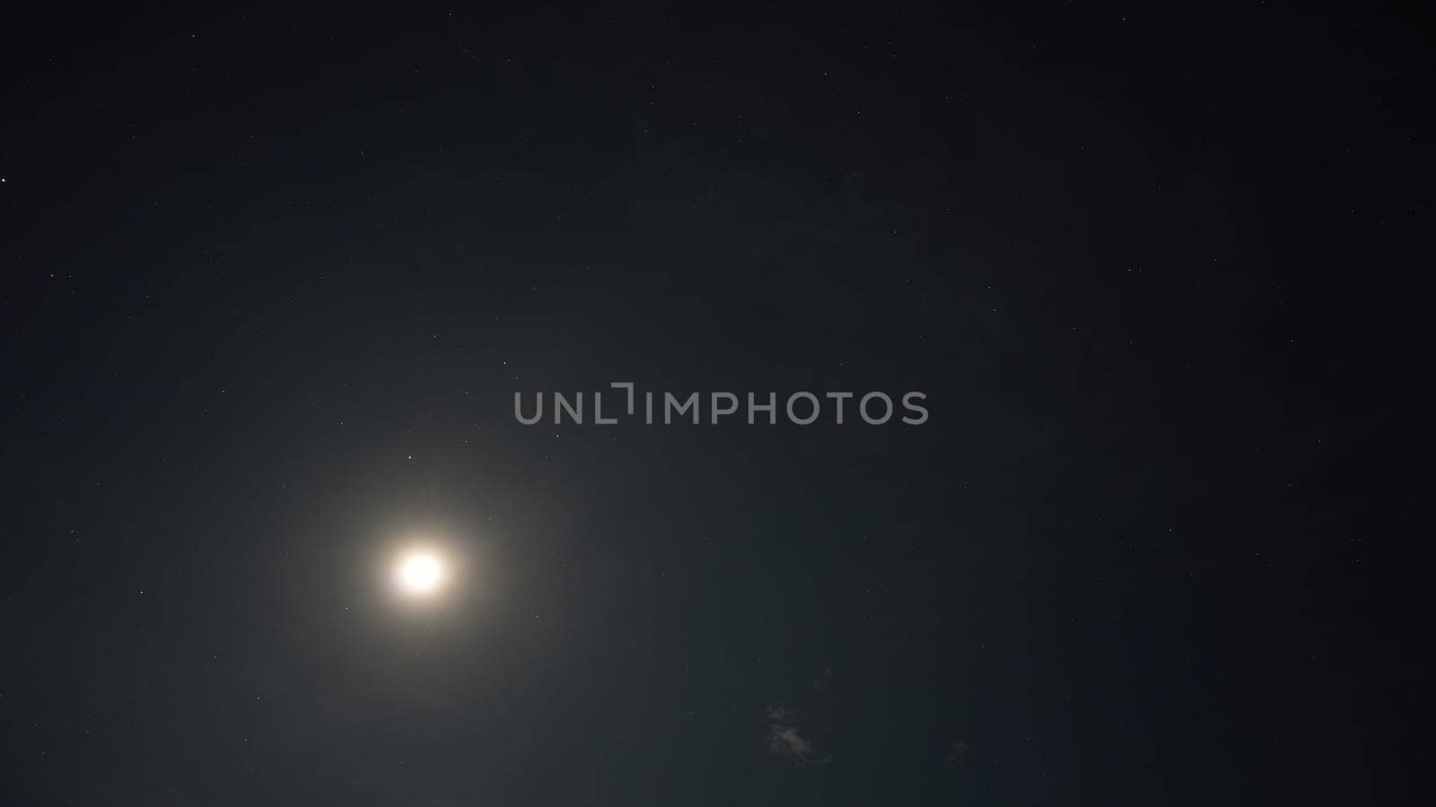Low angle view of a bright moon illuminating the night sky, surrounded by countless twinkling stars, creating a serene and magical atmosphere