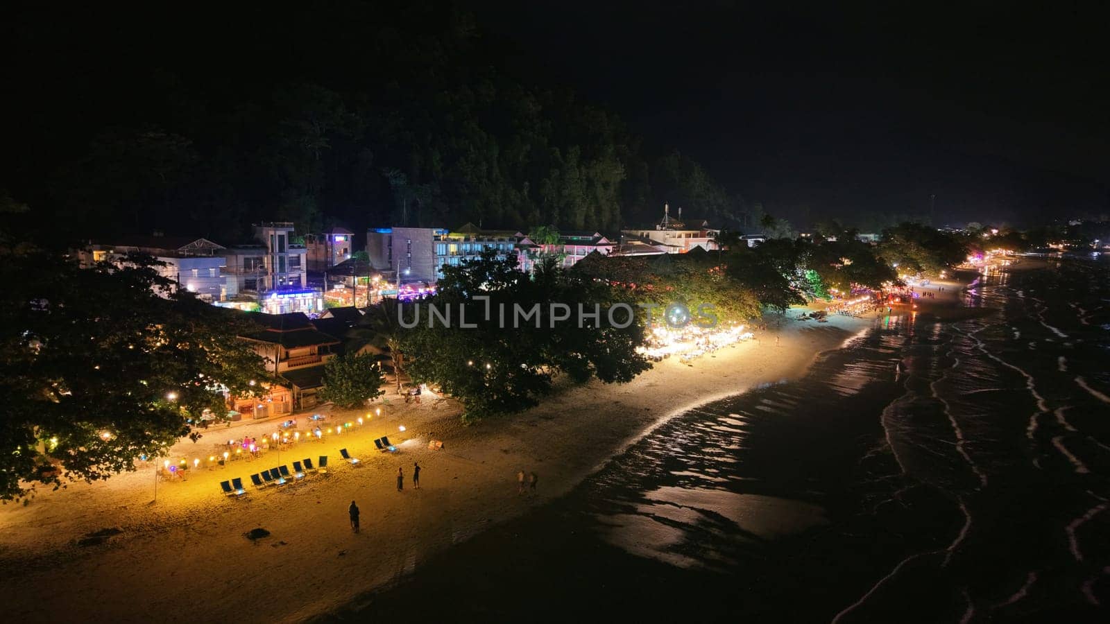 Tourists and vendors mingling at a lively night market on a stunning beach, enjoying a vibrant atmosphere filled with colorful lights and the enticing aroma of street food under the dark sky