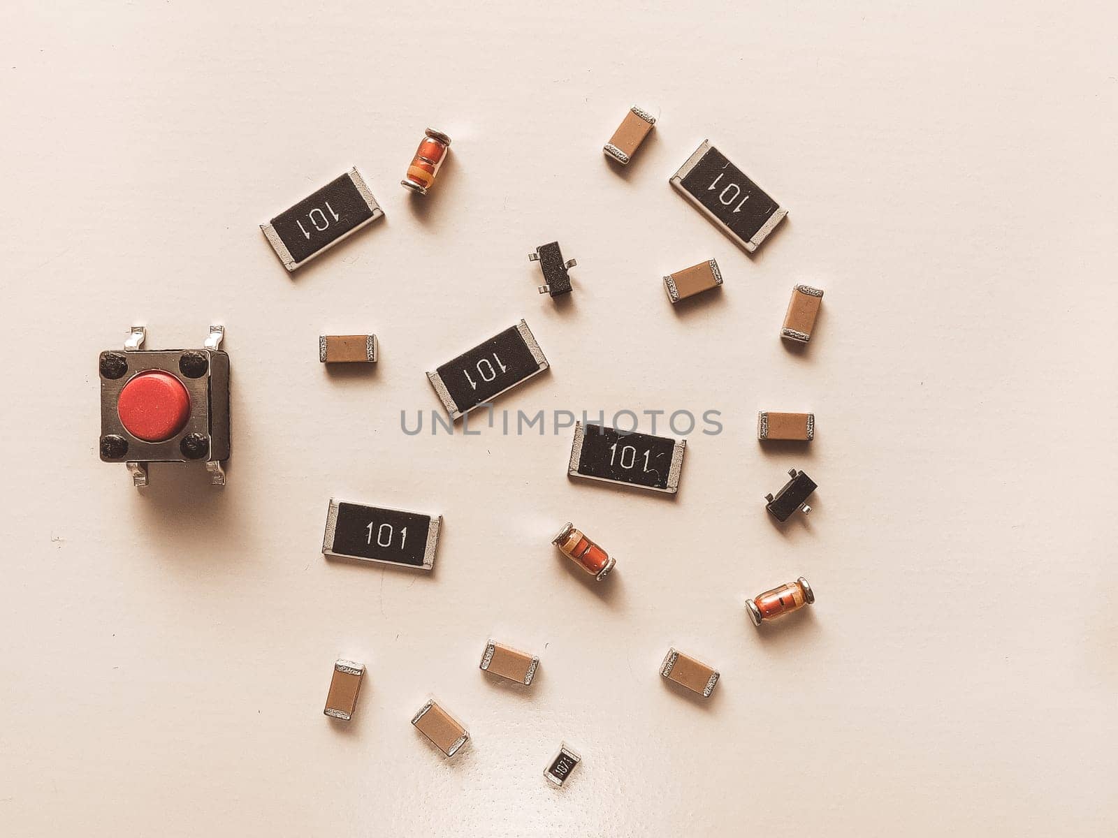 Close-up of various SMD electronic components,diodes, capacitors, and a red tactile push button, arranged on a light background. Ideal for illustrating electronics, DIY tech, and educational materials.