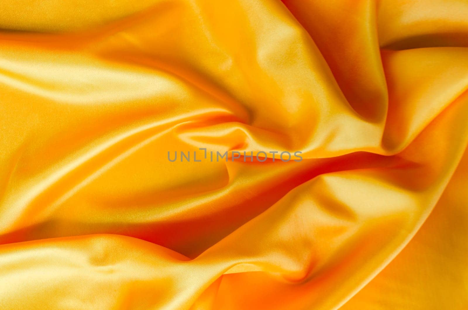 Macro shot of golden silk cloth draped in gentle folds with a polished satin finish