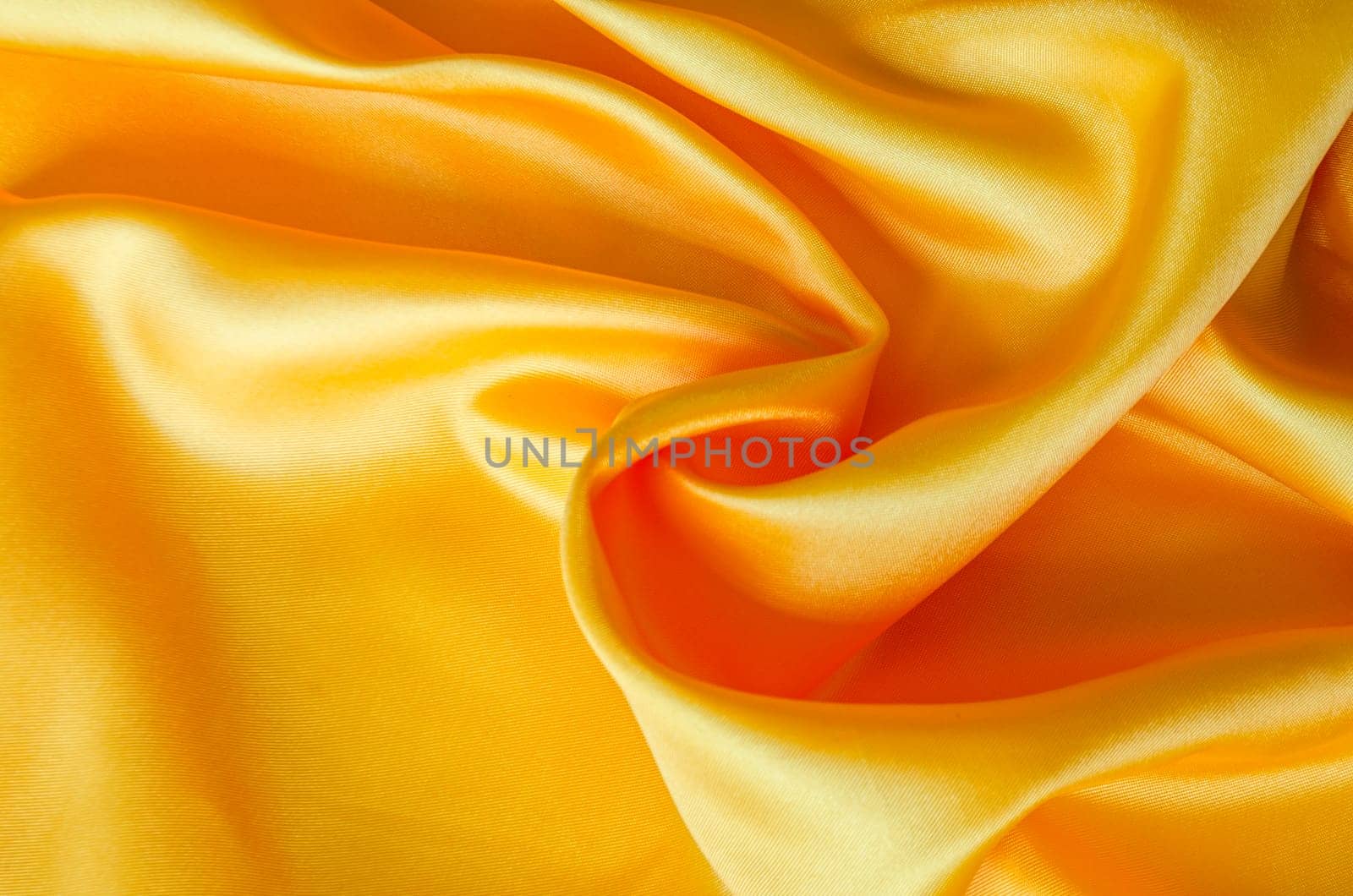 Close up of luxurious golden yellow silk fabric with elegant folds and smooth, glossy surface texture