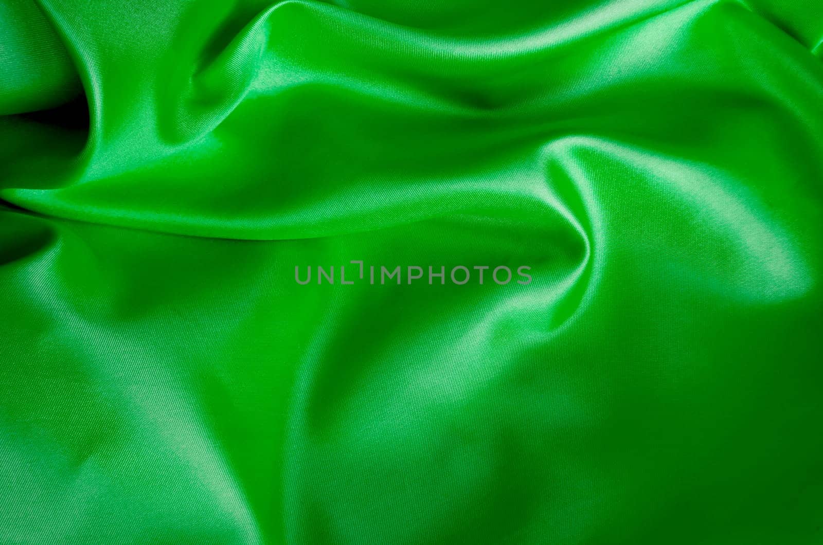 Silky satin fabric in vibrant green with elegant creases and shine. Suitable for design and wallpaper background.