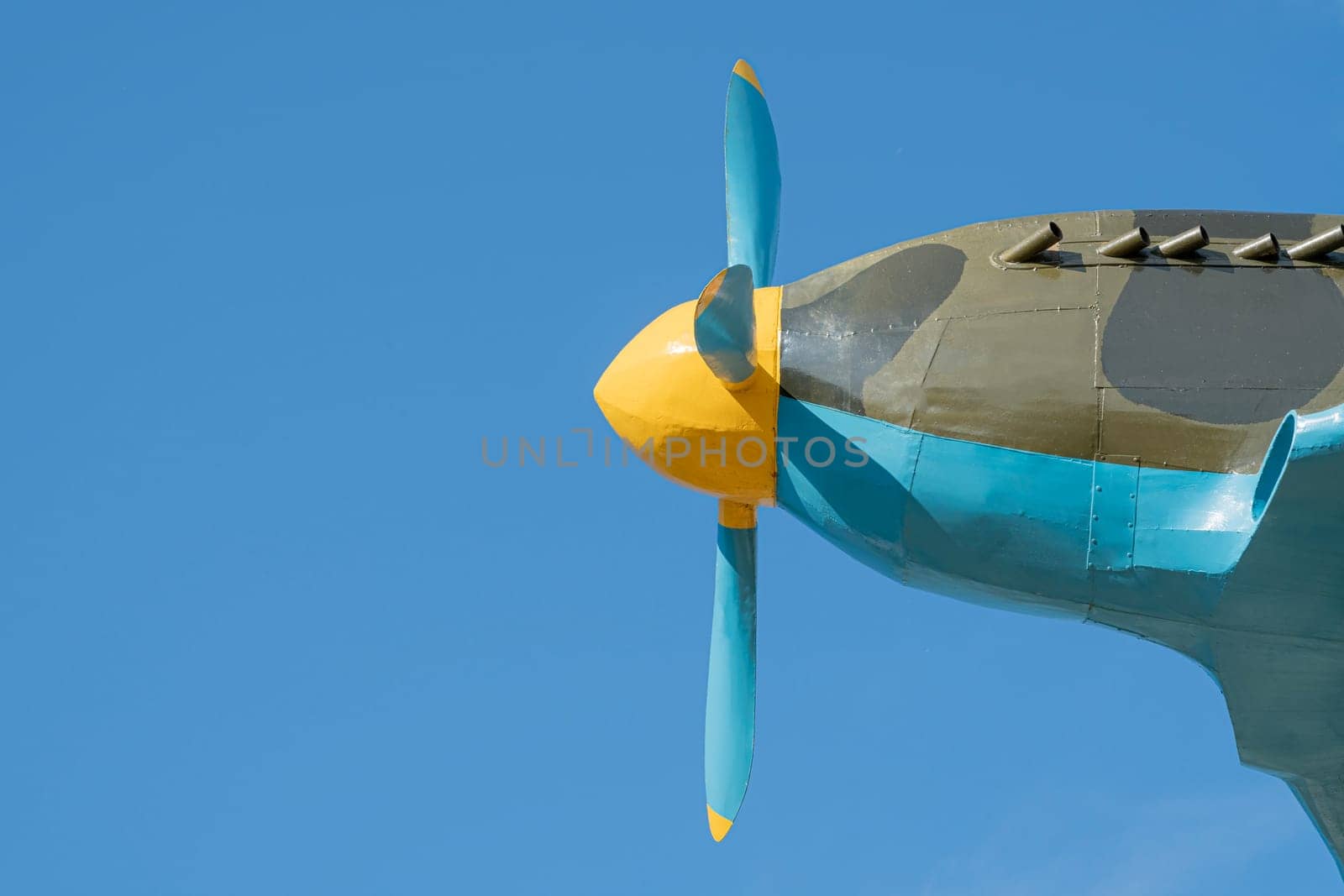 A close-up view of a vintage aircraft's propeller showcasing its colorful design. The bright yellow hub and blue blades stand out against the clear blue sky during daylight.