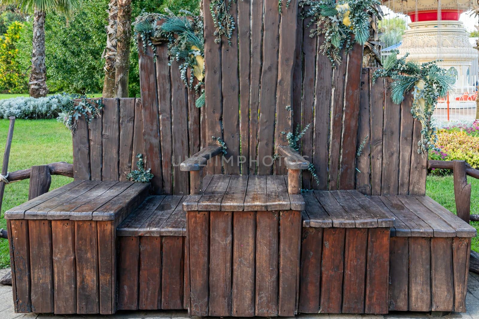 A unique wooden bench with natural foliage embellishment is situated in a vibrant garden. The tranquil atmosphere creates a perfect spot for relaxation among the greenery.