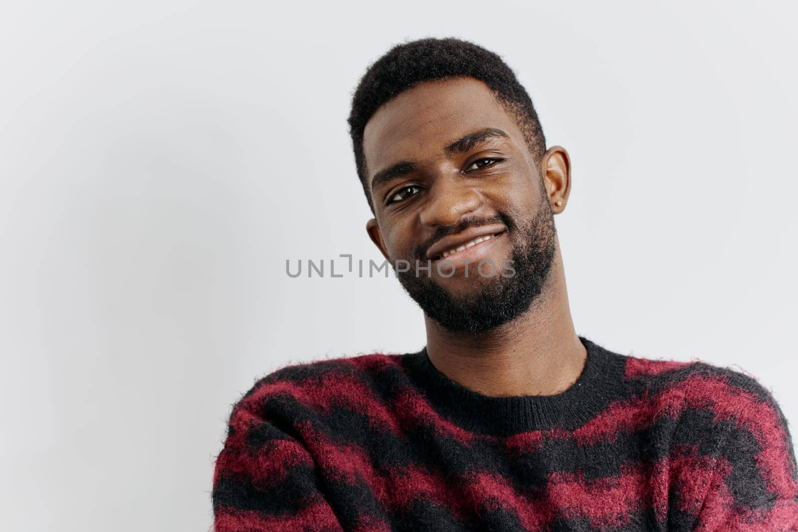 Cheerful man in a vibrant red and black sweater stands confidently against a white background, radiating positivity.